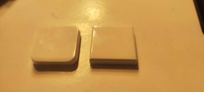 Två små fyrkantiga vita föremål ligger sida vid sida på en ljus yta.