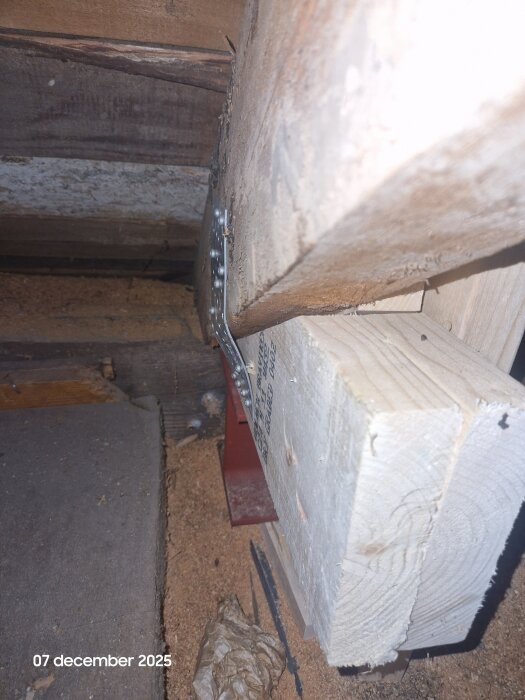 Träbjälkar och metallvinkel sett underifrån, med sågspån och skräp på golvet, i ett byggnadsprojekt.