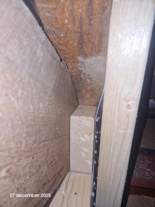 Trästruktur med vinklad balk och monterad metallbeslag mot en vägg, fotograferad närbild.