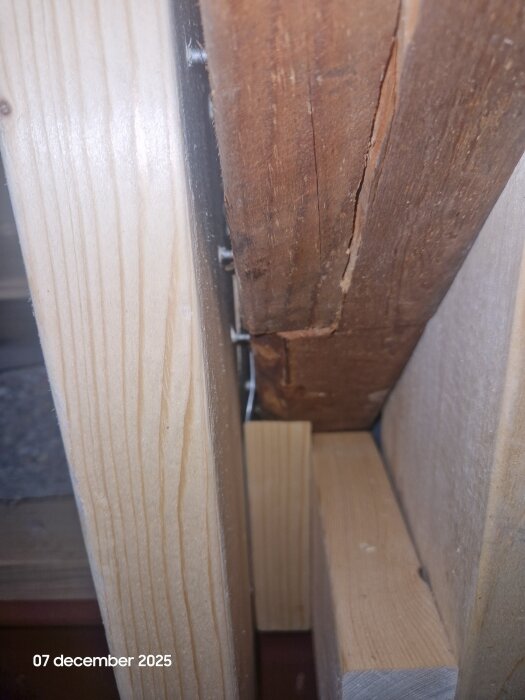 Närbild av träbalkar med sprickor och fästskruvar, visar en konstruktion av trä i ett bygg- eller renoveringsprojekt. Datumet 7 december 2025 syns.