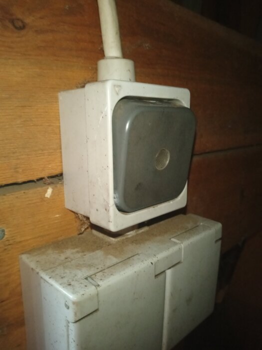 Trasig ljusbrytare i vedbod med dammig yta, kabelanslutning synlig.