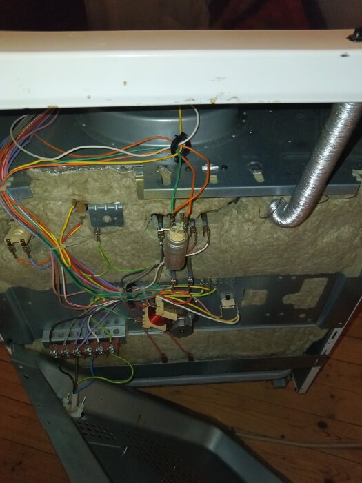 Baksidan av en apparat med synliga kablar, komponenter och isolering monterad på en kylplåt, metallpanel delvis avlägsnad.