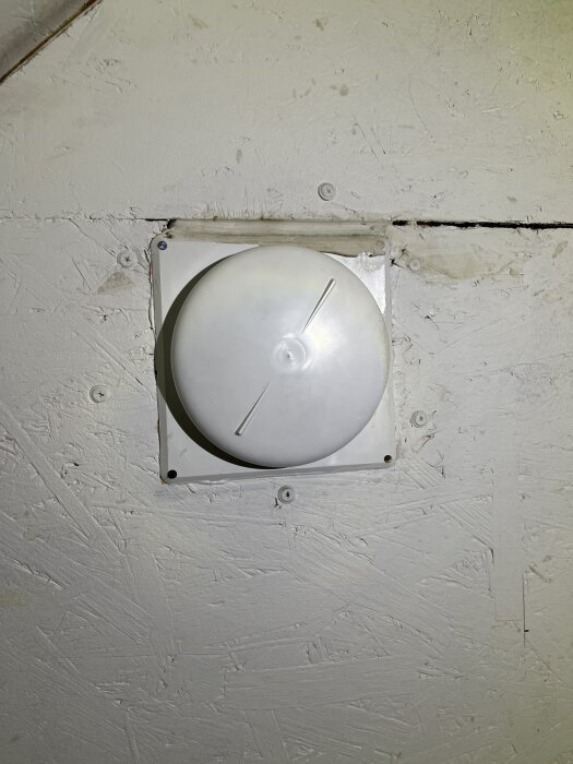 Vit ventilationsventil monterad på en trävägg med synligt slitage.