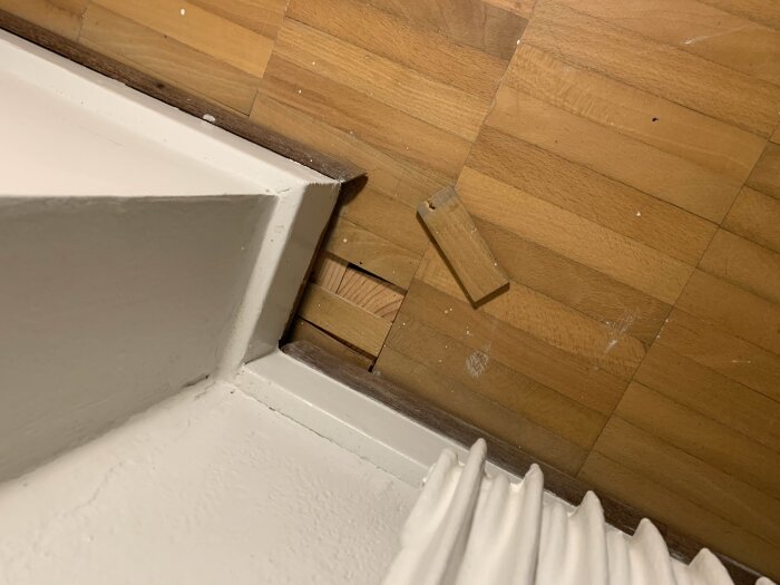 Parkettgolv med glipor vid väggen, träplanka lös. Möjligen byggt 1954, i behov av renovering. Vissa brädor lösa vid vägg och under fönster.