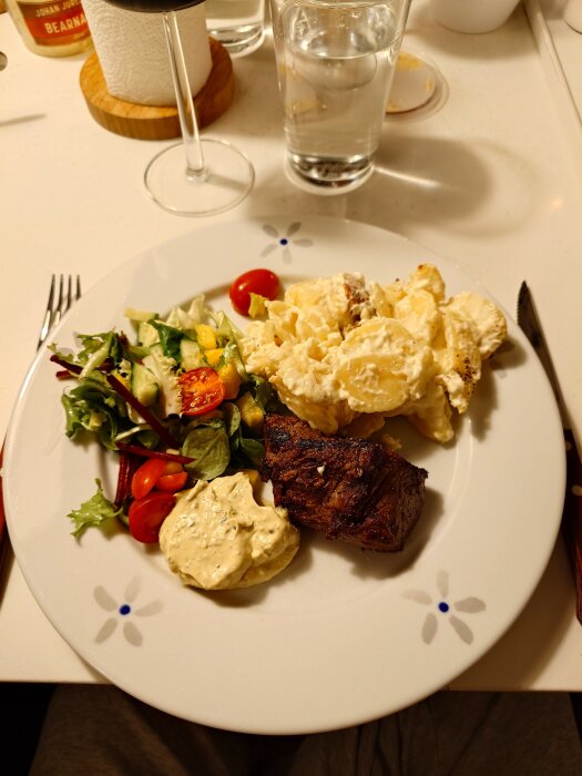 Grillad rostas med potatisgratäng, sallad, tomater och sås på en tallrik.