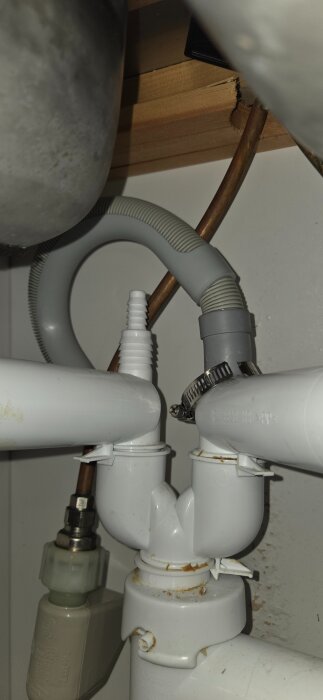 Slang och rör under diskbänk med en lös slangklämma och böjt avloppsrör, potentiell läckagerisk.