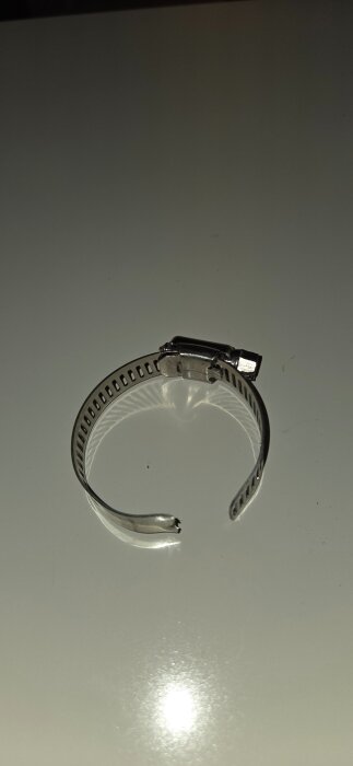 Justerbar metallklämma med skruv, halvcirkelformad på vitt underlag.