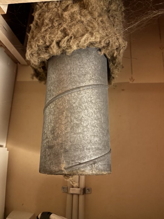 Ett ventilationsrör med isolering ovanför spishällen, där luft blåser ut istället för att sugas in.