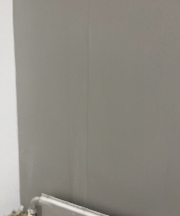 Ojämn spackling och målning på vägg i hall, med bubblor och knottror synliga.