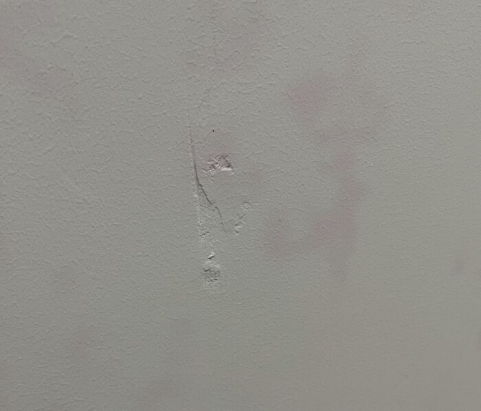 Närbild av ojämn väggyta med färgade fläckar och synliga bubblor samt sprickor efter spackling och målning.