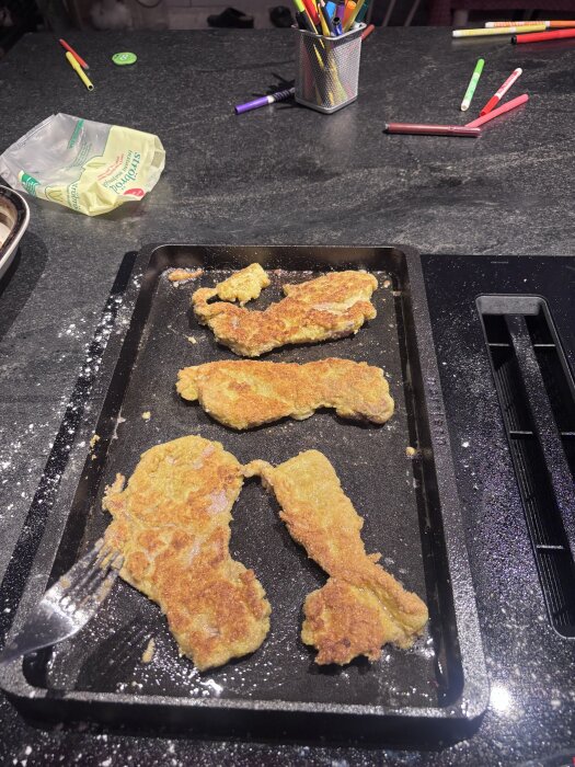 Stekt fläskschitzel på en häll med jämn värme, omgiven av diverse köksredskap och förpackningar, efter diskning med diskborste och varmt vatten.