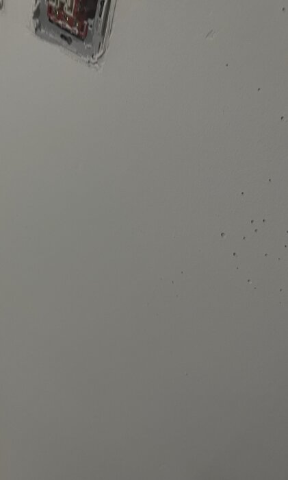 Vägg med ojämnheter och bubblor efter första lagret färg; ett eluttag syns delvis.