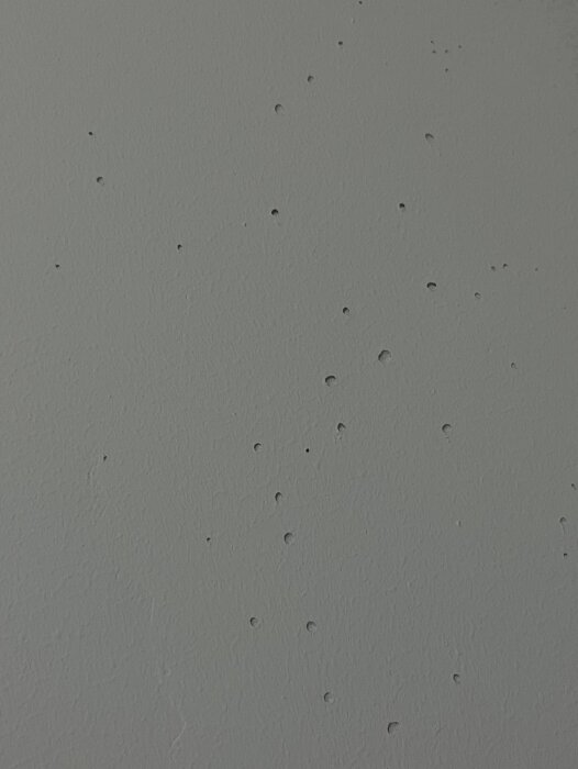 Ojämn spacklad väggyta med synliga hål och bubblor i grått målat rum.