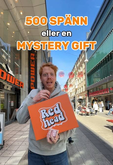 Person håller en orange låda med texten "Red head" på en stadsbutiksgata. Text på bilden: "500 spänn eller en mystery gift".