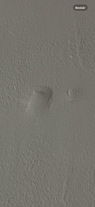 Betongvägg med synliga bucklor och silvriga ringar, troligen pluggrelaterat problem vid renovering.