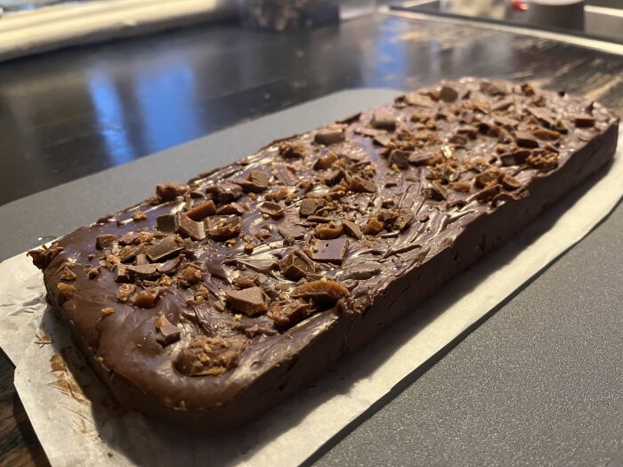 Hemmagjord daimfudge på bakplåtspapper, täckt med hackad choklad och kolabitar.