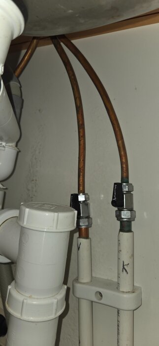 Under diskbänk med synliga vattenrör och rördelar, inklusive kopparrör och vita plastkopplingar.