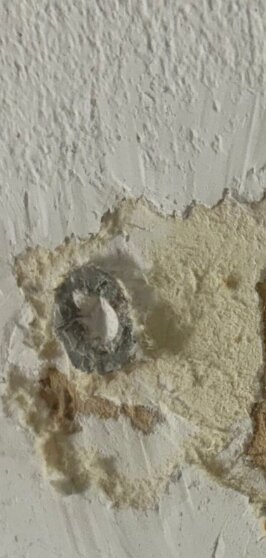 Vägg med skadad yta där en plugg syns.