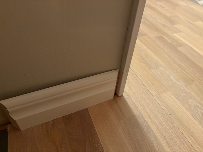 Vit golvlist och tröskel vid dörrkarm på ett trägolv.