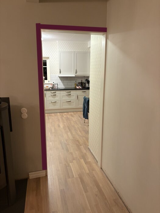 Öppen dörröppning med markerad dörrpost i lila, visar övergång mellan korridor och kök. Fråga om listdesign och dess ände mot väggen.