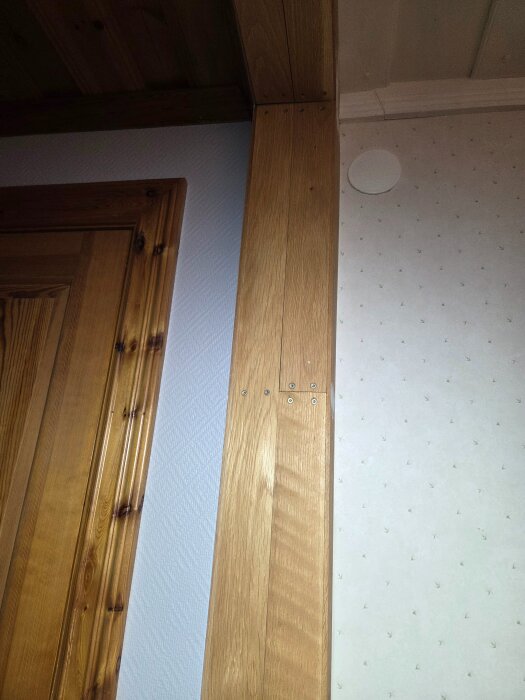 Träpanel och dörrkarm i en inomhusmiljö, potentiellt en gammal innervägg mellan kök och allrum.