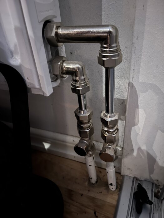 Rörsystem i ett hem med blanka och vita rör anslutna till en radiator i hallen, med fokus på rörens installation och anslutningar.