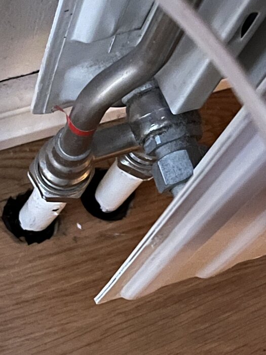 Rörsystem vid golv med synliga vita och blanka rör i hallen, kopplat till ett element.