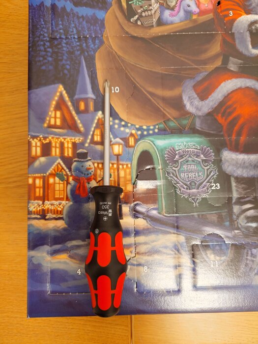 Skruvmejsel placerad på tecknad julkalender med motiv av snögubbe, jultomte och hundsläde.