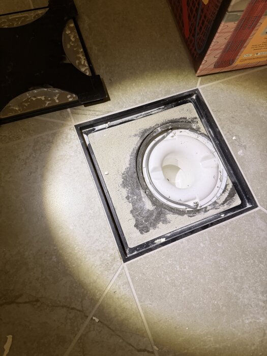 Golvbrunn installerad i badrumsgolv, med kakel och tätskikt runtomkring, lyses upp av en ficklampa.