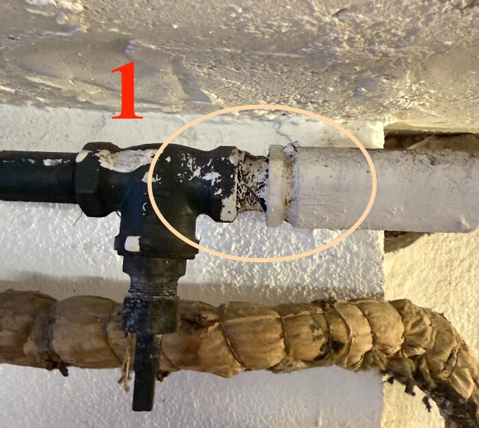 Gammalt galvat rör kopplat till vitmålat rör, märkt "1", i en källare. Rören är gamla och i behov av uppgradering.