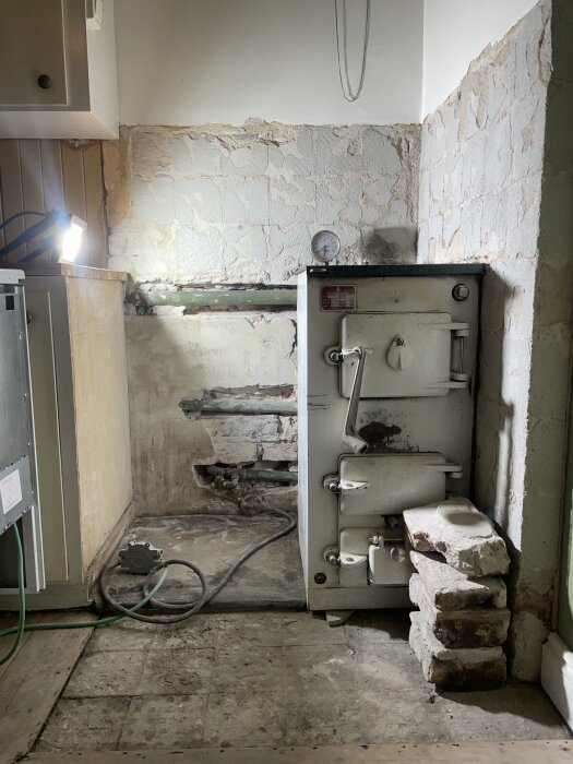 Gammal kökspanna Norrahammar 300 från 1963 med anslutna rör och slitna väggar, omgiven av lösa tegelstenar, i ett nergånget kök.