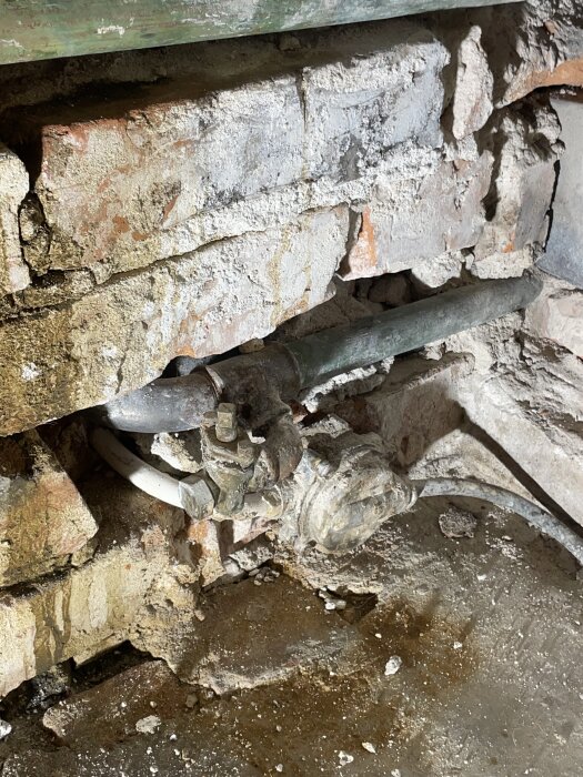 Gammal tegelvägg med ett metallrör, anslutningar och slangklämmor, del av ett äldre värmesystem.