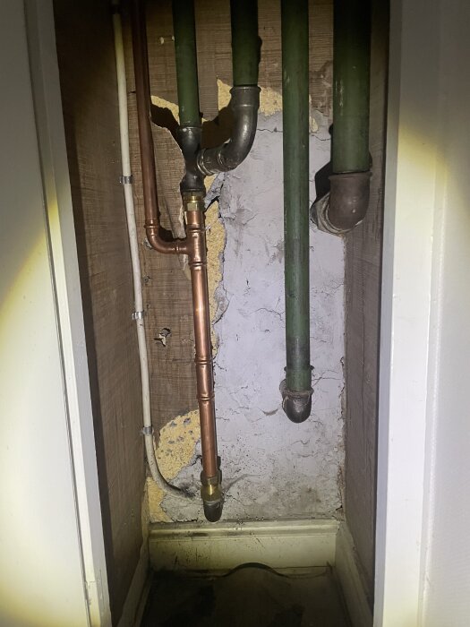 Koppar- och järnrör i ett skåp markerade som en del av radiatorkretsen, med slitage på väggen bakom rören.