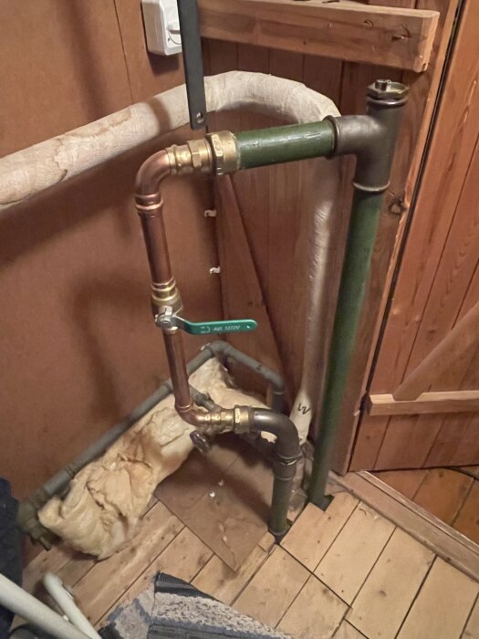 Rörsystem i ett skåp med koppar- och stålledningar samt ventiler. Isolering syns på vissa rördelar. Trägolv och väggar i bakgrunden.