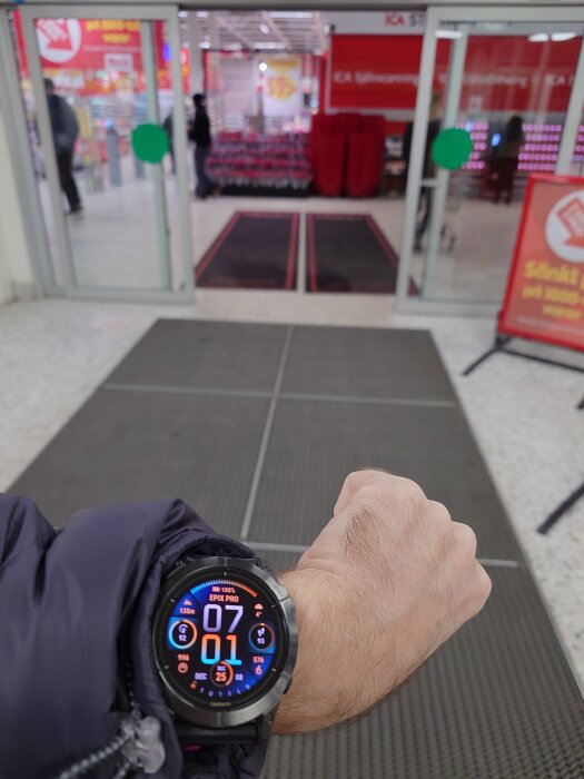 Hand med klocka framför entré till livsmedelsbutik, tiden visar 07:01.