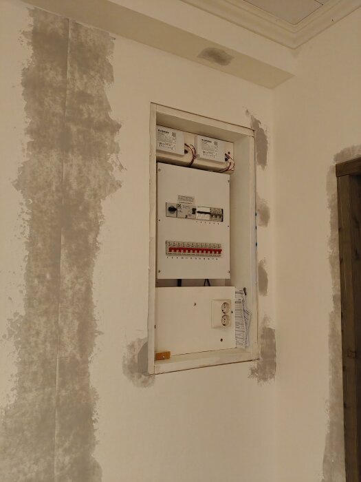 Elcentral på väggen med inspektionslucka, omgiven av ofullständig tapetsering med mönsteranpassad tapet där tapetfinishen diskuteras.