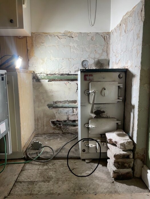 Gammal kamin i ett slitet rum med avskalade väggar och trasigt golv, omgiven av gamla tegelstenar och lösa kablar.