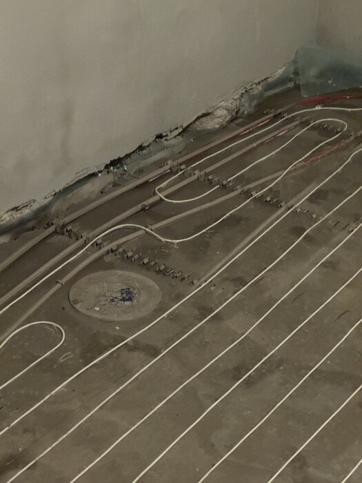 Rörinstallationer och golvvärmeslingor med flytspackel i källarbadrum under renovering, nära golvbrunn.