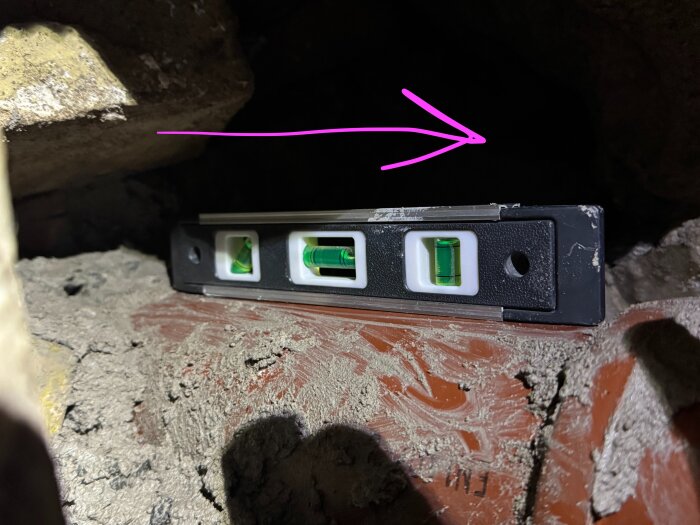 Vattenpass på mursten visar lutning, rosa pil indikerar riktning höger.