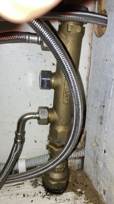 Vattenfördelare med tre anslutningar, varav en är oanvänd. Kopparrör och armerade slangar synliga i ett trångt utrymme under diskbänken.