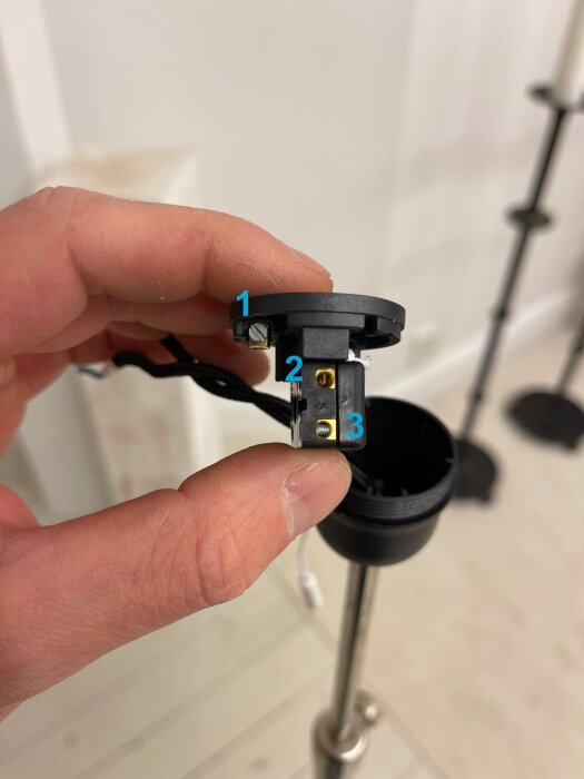Närbild av en lamphållare med dragströmbrytare. Tre ingångar numrerade 1, 2 och 3 syns tydligt. En hand håller i hållaren.