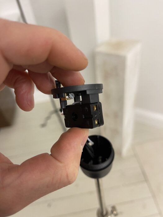 Hand håller en lamphållare beställd från Italien, nära en lampa under installation. Frågor om jorden och kopplingar nämns i texten.