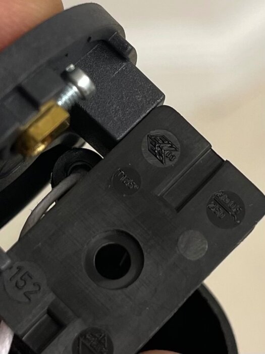 Svart plastkomponent av en italiensk lamphållare med märkningar och en skruv synlig.