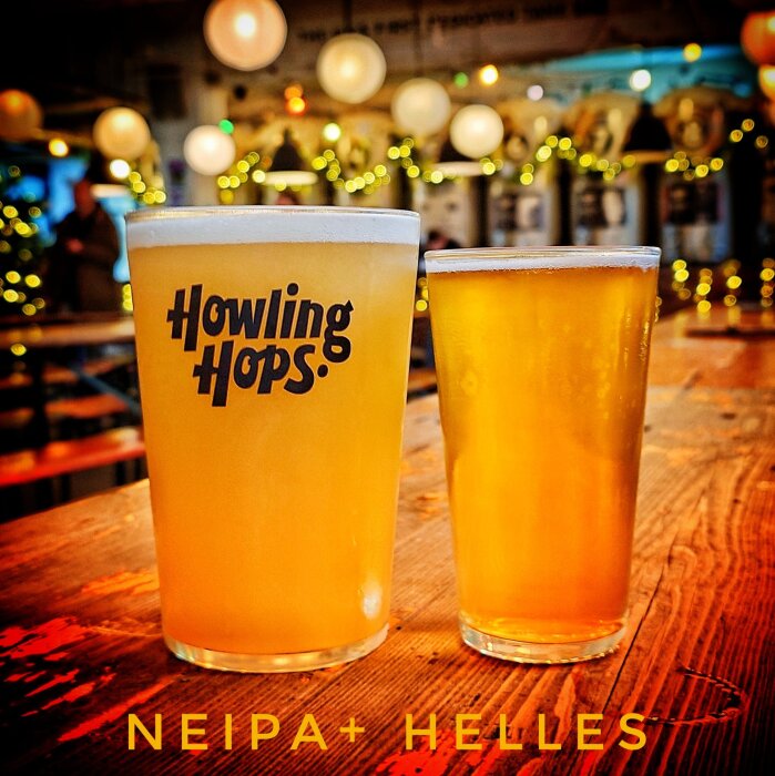 Två ölglas på ett träbord, ett med texten "Howling Hops," i en upplyst miljö med dekorationer i bakgrunden.
