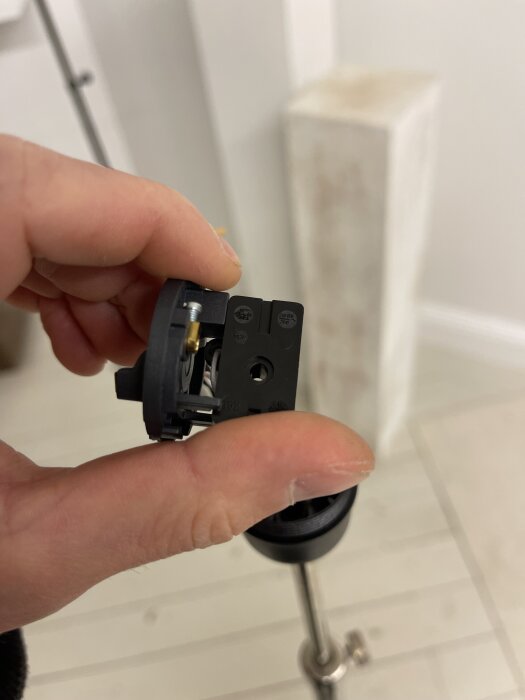 Närbild av en person som håller en svart lamphållare i handen, visar elektriska anslutningar i ett rum med ljusa trägolv i bakgrunden.