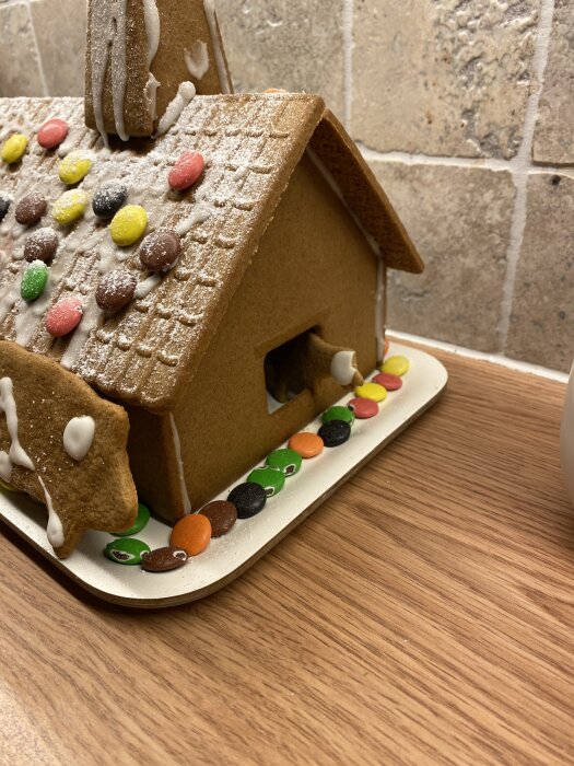 Pepparkakshus dekorerat med färgglada godisar och florsocker på ett träbord framför en stenvägg.