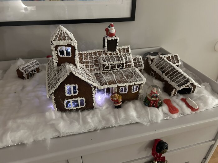 Pepparkakshus med kristyr och lakritsdetaljer, inkluderande en studsmatta, inspirerat av ett riktigt hus, dekorerat med små jultomtar och snölandskap.