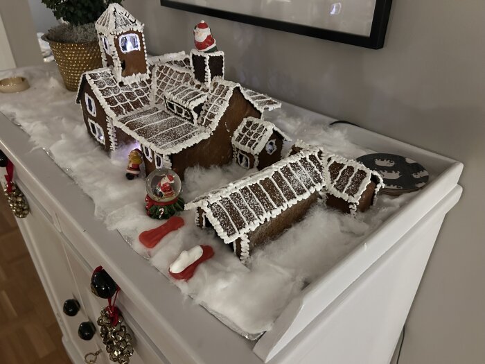 Pepperkakshus med detaljrik dekor av kristyr, inklusive pepparkakstak och en liten lakritsstudsmatta, på ett bord med vintertema.