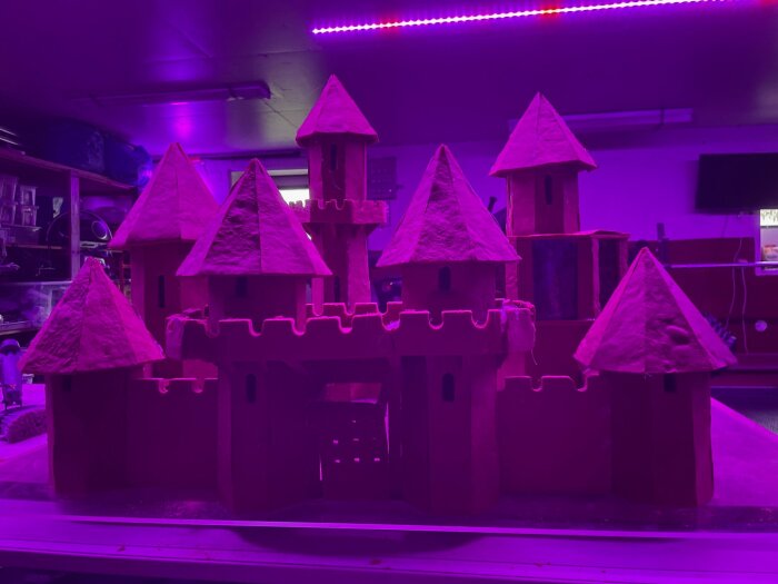Pepparkaksslott med flera torn, upplyst av lila LED-ljus i ett rum.