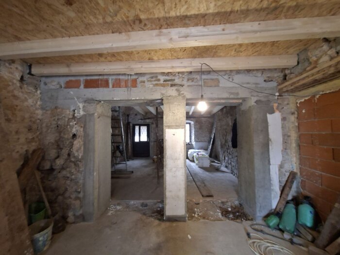 Renoveringsprojekt med nyöppnade dörröppningar mellan kök och vardagsrum, oskyddade väggar, en stege, och byggmaterial i bakgrunden.